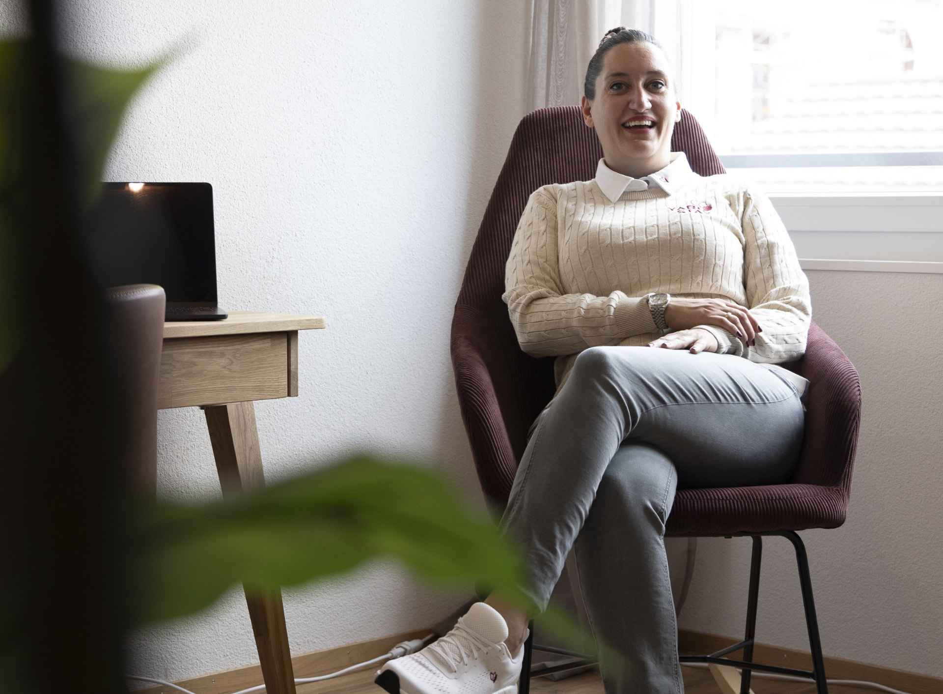 Sibille Hablützel, Mitgründerin von Yari Stay, sitzt lächelnd in einem burgunderfarbenen Sessel in einem hellen, modern eingerichteten Raum mit Tageslicht vom Fenster