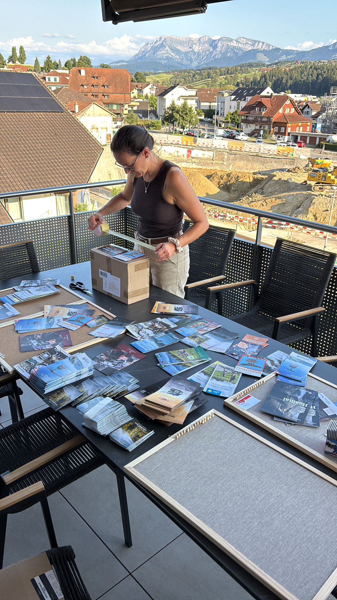 Marianne sortiert Gäste-Flyer auf dem Balkon mit Blick auf die Berge